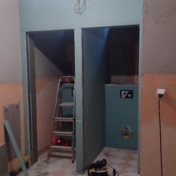 IZO-PLUS PAWEŁ WALSKI - Wnętrze w trakcie remontu: ściany z płyt karton-gips, drabina, narzędzia i przewody na podłodze w kratkę. Widoczne elementy instalacji.