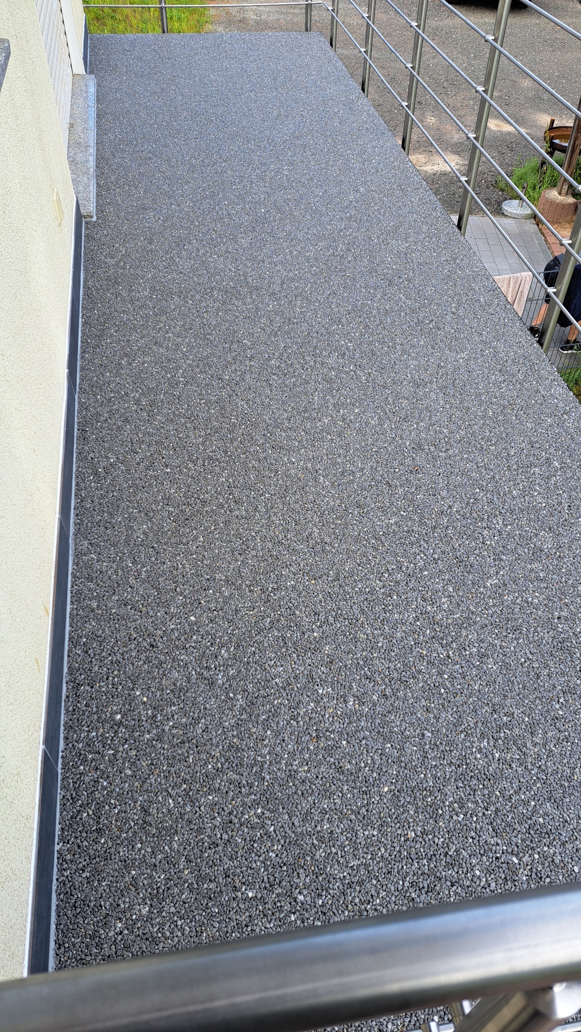 Szara, kamienna nawierzchnia balkonu z metalową balustradą, przylegająca do ściany budynku. Widoczne detale wykończenia i faktura kamienia.