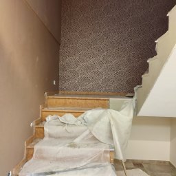 Janusz Zuzelski Uslugi Ogolnobudowlane - Ściana z tapetą o wzorze koncentrycznych okręgów w brązowych odcieniach, fragment schodów zabezpieczonych folią malarską podczas prac wykończeniowych.