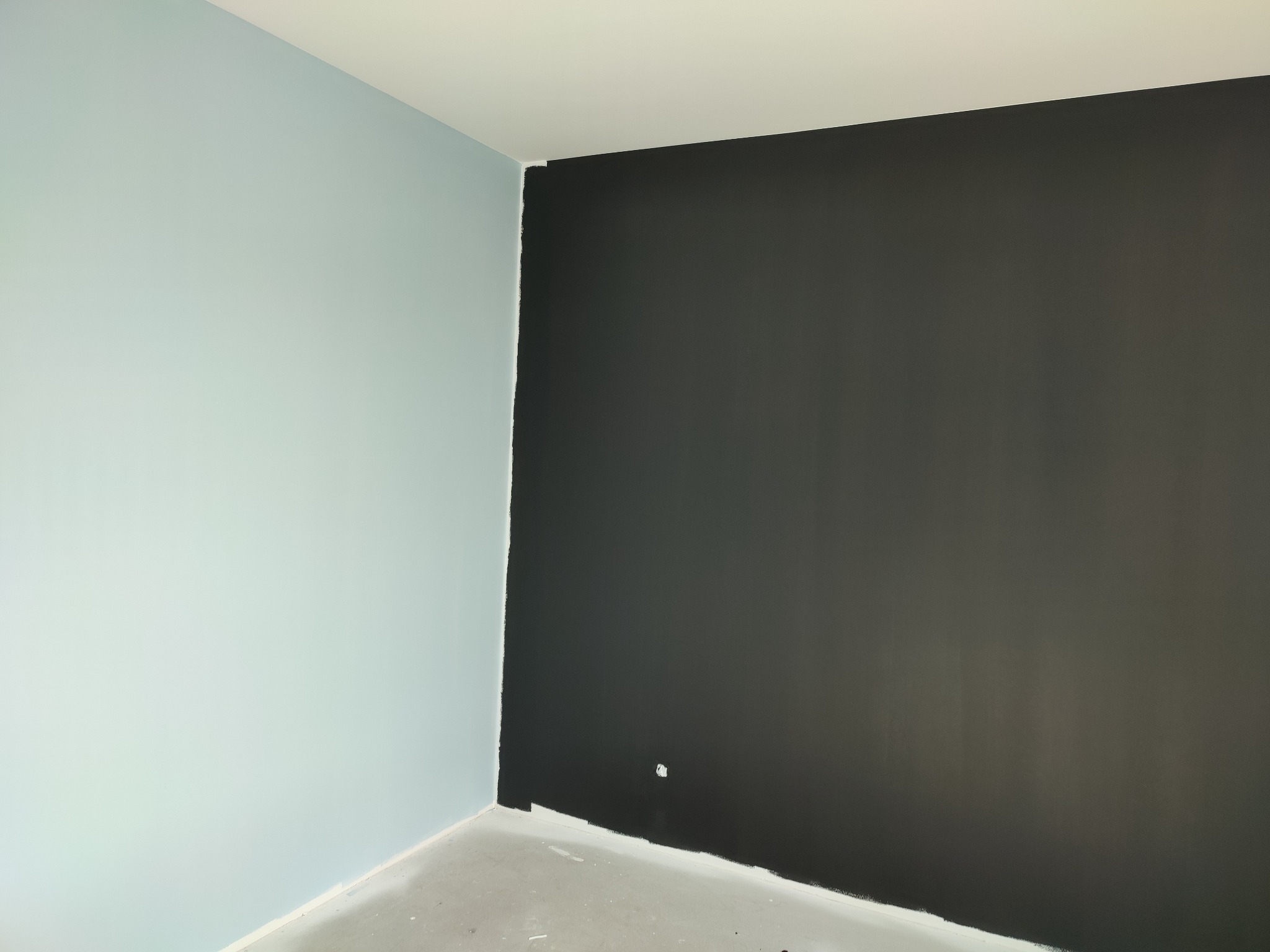 Pomieszczenie po malowaniu: jedna ściana w kolorze błękitnym, druga pomalowana na czarno, widoczne niedociągnięcia przy podłodze.