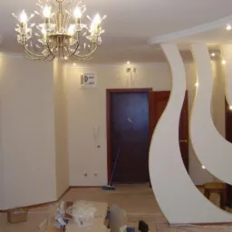 Wnętrze po remoncie: faliste ścianki działowe z oświetleniem punktowym, kremowe ściany, żyrandol. Widoczne ślady prac wykończeniowych.