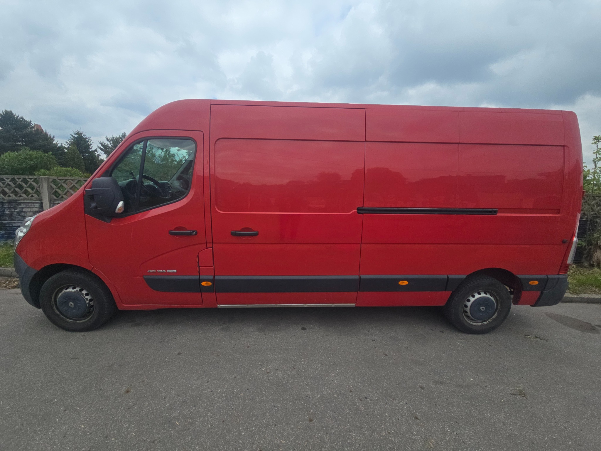 Czerwony bus Renault Master z Chorzowa, zaparkowany na ulicy. Widok z boku, pochmurne niebo w tle. Auto gotowe do transportu.