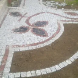 Ozdobny wzór z kostki granitowej na ścieżce w Wałbrzychu. Detal kompozycji z motywem roślinnym, z użyciem szarej i czarnej kostki. Częściowo widoczne krawędzie.