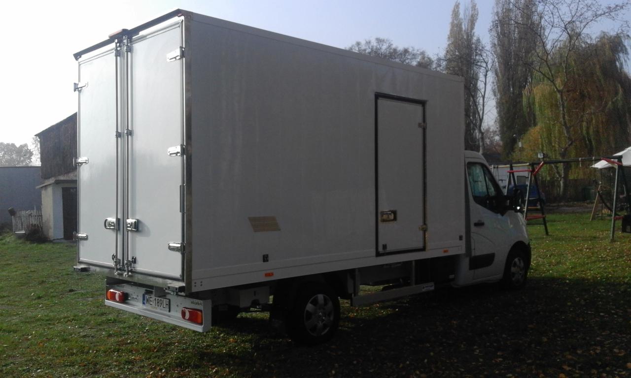 Biały bus z zabudową kontenerową, widok z tyłu, na zielonym trawniku. Widoczne drzwi kontenera i dodatkowe drzwi boczne. Tablica rejestracyjna WE 189LH.
