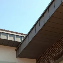 Nowoczesne, grafitowe poszycie dachu z blachy na budynku z cegły klinkierowej, widoczne logo producenta na dachu.