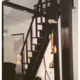 Czarna konstrukcja z drewnianych schodów i antresoli w pokoju z ciemną podłogą i przedmiotami na ścianie