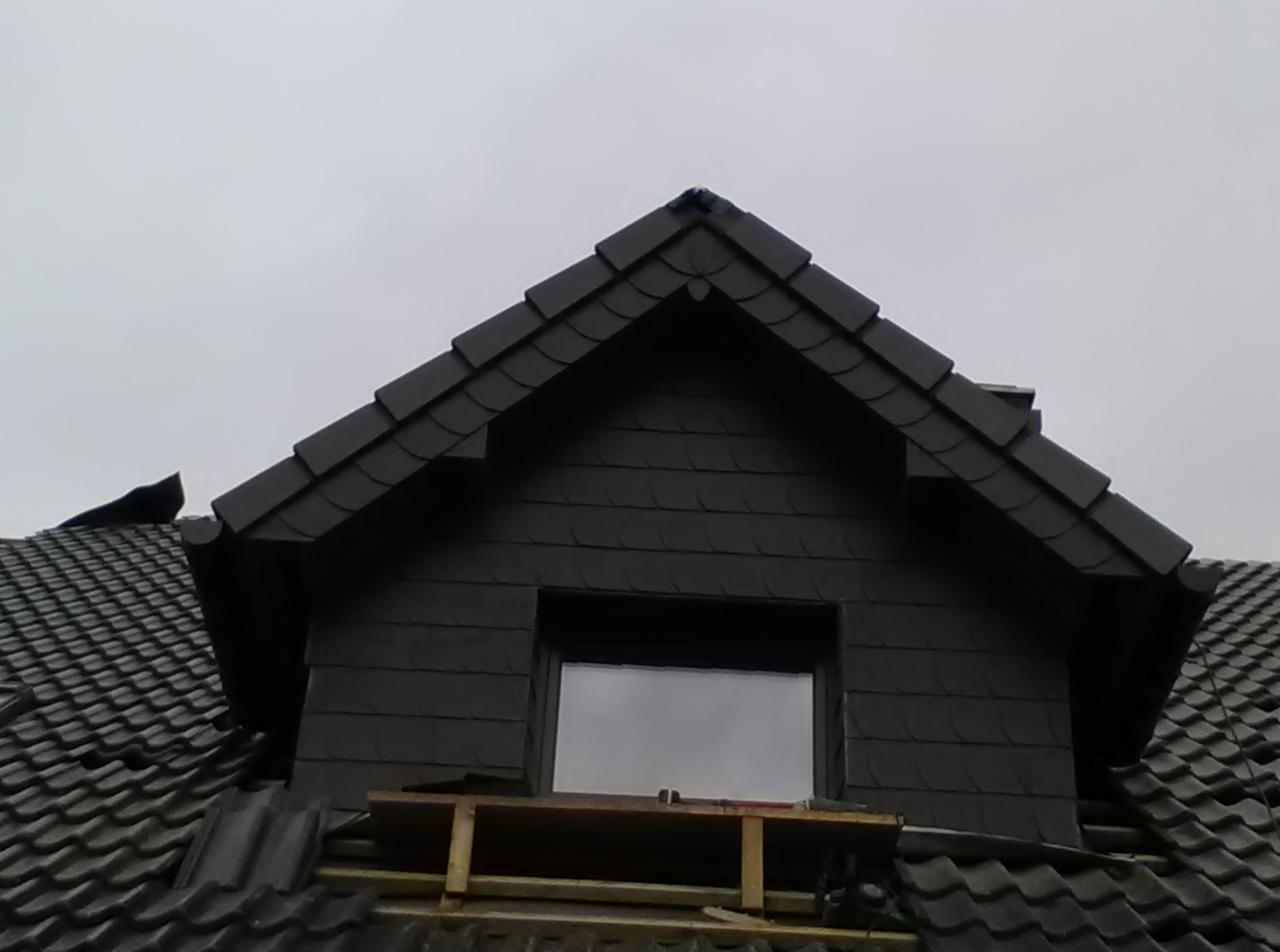 Ciemny dach z łupka z oknem dachowym i drewnianą konstrukcją pomocniczą. Fragment dachu z widoczną rynną. Pochmurne niebo w tle.