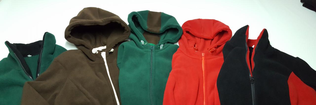 Różnokolorowe bluzy polarowe z kapturem, zapinane na zamek, ułożone obok siebie na białym tle. Widoczne detale: sznurki, zamki błyskawiczne, wykończenia kapturów.