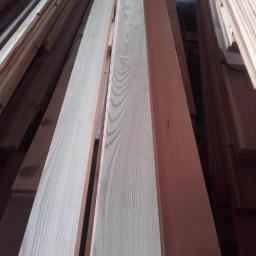 Skansa - Jasne deski z wyraźnym rysunkiem słojów, ułożone w stos. Widoczne krawędzie i faktura drewna. Ujęcie z dołu podkreśla długość materiału.