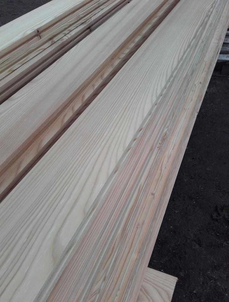 Jasne, surowe deski ułożone warstwami, widoczny rysunek drewna, przygotowane do dalszej obróbki na zewnątrz.