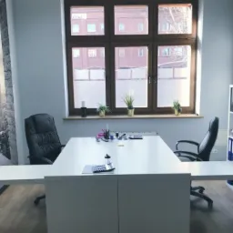 Jasne biuro z dużym oknem i biurkiem, fototapeta z panoramą miasta, regał z segregatorami, dwie czarne skórzane krzesła biurowe.