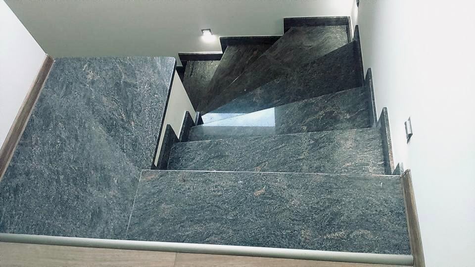 Wewnętrzne schody z ciemnego kamienia z widoczną fakturą, oświetlone punktowym światłem sufitowym, z metalową listwą na krawędziach stopni.