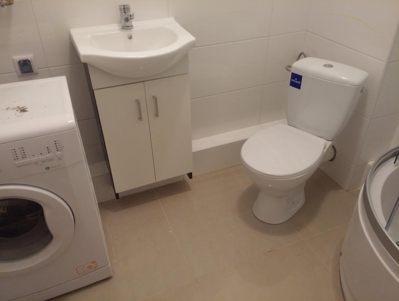 Wykończona łazienka z białą umywalką z szafką, toaletą Cersanit i pralką, wykończenie pod klucz.