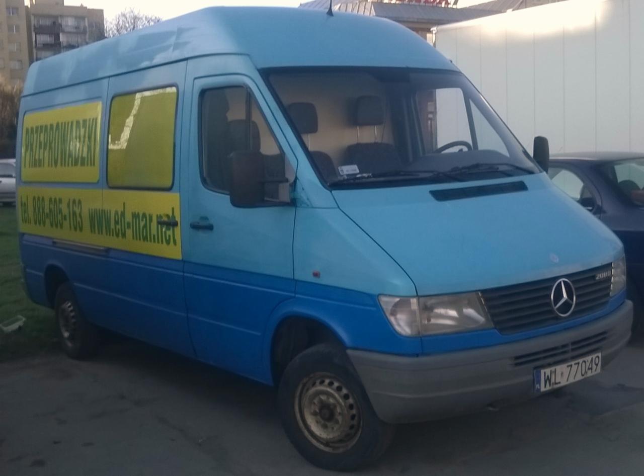 Niebieski bus Mercedes Sprinter z żółtym napisem 'Przeprowadzki' i danymi kontaktowymi firmy. Widoczny numer rejestracyjny WL 77049.
