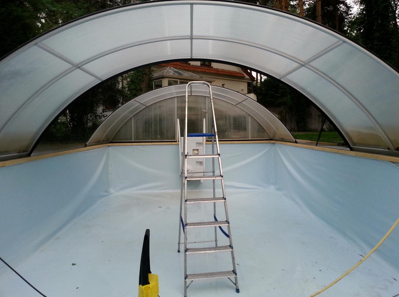 Pusty basen z metalową drabinką i zadaszeniem z poliwęglanu. Na dnie basenu widoczne ślady po wodzie i żółty odkurzacz. W tle dom z czerwonym dachem.