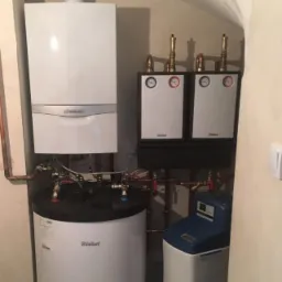 Zestaw urządzeń grzewczych w kotłowni: wiszący piec gazowy Vaillant, zasobnik ciepłej wody z czarnym wiekiem, dwa moduły sterujące Dieder i zmiękczacz wody.