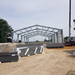 EUROBEX SPÓŁKA Z OGRANICZONĄ ODPOWIEDZIALNOŚCIĄ - Stalowa konstrukcja hali w trakcie budowy, na placu budowy leżą płyty warstwowe, w tle widoczny dźwig, Sochaczew.