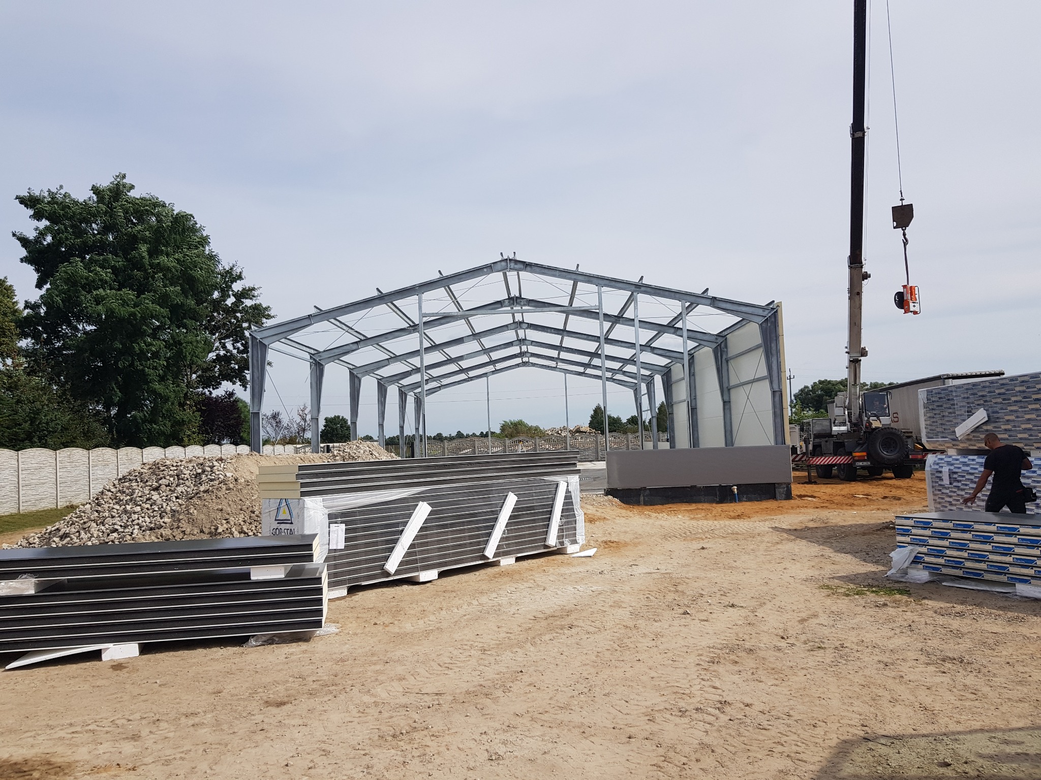 Stalowa konstrukcja hali w trakcie budowy, na placu budowy leżą płyty warstwowe, w tle widoczny dźwig, Sochaczew.