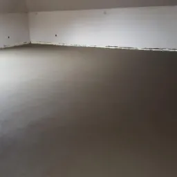 Świeżo wylana, gładka posadzka w pomieszczeniu w Nowym Żmigrodzie, przygotowana do dalszych prac wykończeniowych, widoczne zabezpieczenia przy ścianach.