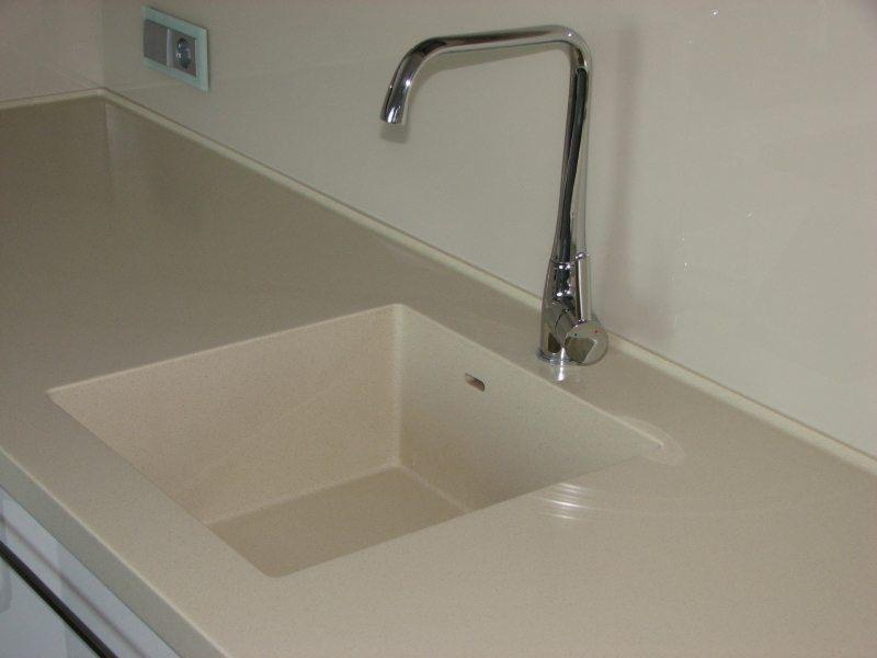 Beżowy blat kuchenny z wbudowanym zlewem i chromowaną baterią, widoczny fragment gniazdka elektrycznego w tle.