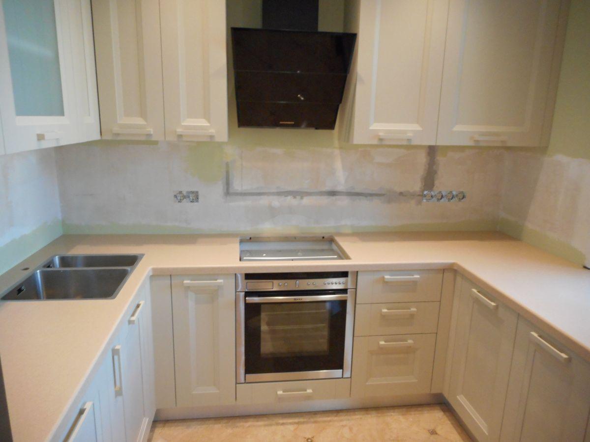 Montaż jasnej zabudowy kuchennej z płytą grzewczą i piekarnikiem w trakcie wykończenia, widoczne gniazdka elektryczne na ścianie.