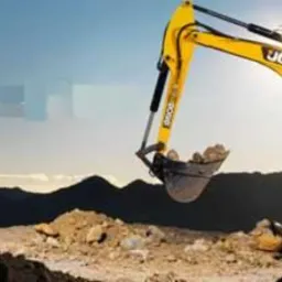 Żółto-czarna koparka JCB nabiera ziemię do żółtej przyczepy na tle wzgórz i błękitnego nieba. Operator w kabinie.