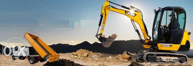 Żółto-czarna koparka JCB nabiera ziemię do żółtej przyczepy na tle wzgórz i błękitnego nieba. Operator w kabinie.