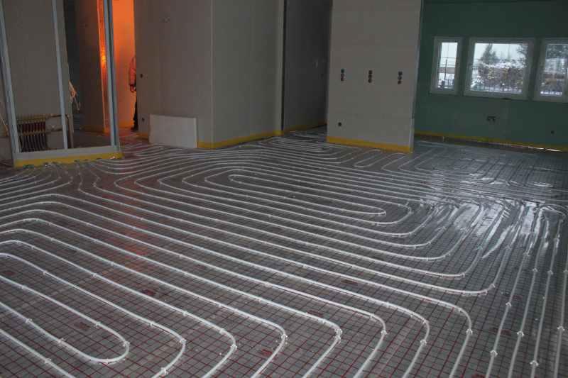 Ułożone rury ogrzewania podłogowego na siatce w surowym wnętrzu, przygotowane do wylewki. Widoczne zabezpieczenia ścian taśmą.