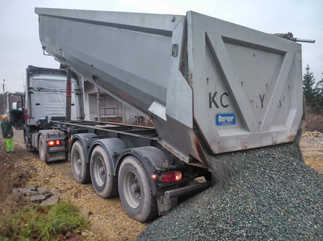 Ciężarówka wywrotka z otwartą skrzynią, wysypująca żwir. Widoczny pracownik w odblaskowej odzieży. Usługi transportowe Libiąż.