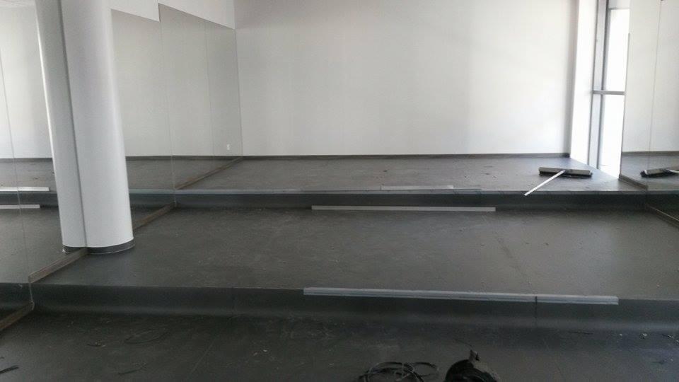 Przygotowanie podłoża pod posadzkę w przestronnym, jasnym pomieszczeniu z kolumną i lustrami na ścianach. Widoczne listwy przypodłogowe i narzędzia.