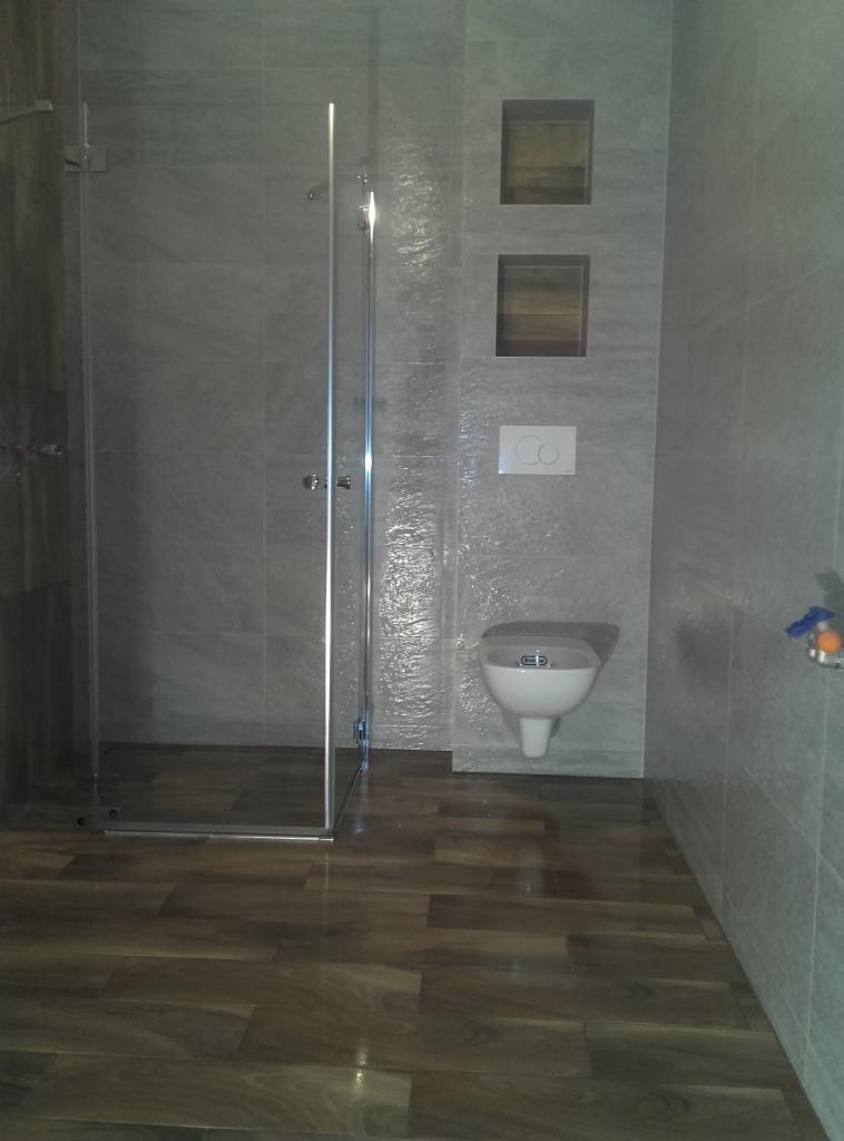 Nowoczesna łazienka z kabiną prysznicową typu walk-in, wykończona szarą płytką imitującą kamień i drewnopodobną podłogą. Widoczne wnęki w ścianie.