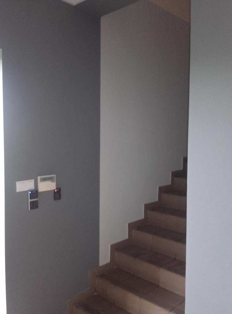 Klatka schodowa po malowaniu ścian na szaro, z widocznymi schodami wyłożonymi płytkami i zamontowanym systemem kontroli dostępu.
