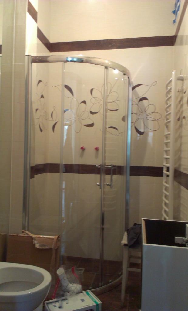 Wykończona kabina prysznicowa z dekoracyjnymi wzorami kwiatowymi na szklanych ściankach, zamontowana w łazience z beżowymi płytkami i brązowymi akcentami.