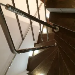 Spiralne schody wykończone płytkami imitującymi drewno, z metalową, chromowaną balustradą i poręczą, widok z góry.