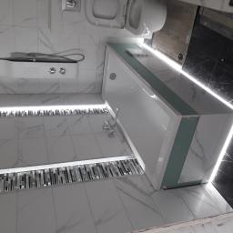 Pcu horyzont - Nowoczesna łazienka z białymi płytkami imitującymi marmur, podświetlanymi listwami przypodłogowymi z mozaiki, białą wanną z zielonym obramowaniem i czarną ścianą w tle.