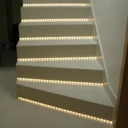 Schody wykończone jasnym drewnem z wbudowanym oświetleniem LED na każdym stopniu, tworzące efektowny wizualnie element dekoracyjny.