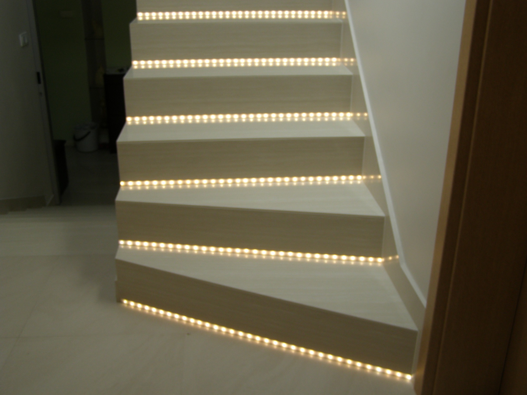 Schody wykończone jasnym drewnem z wbudowanym oświetleniem LED na każdym stopniu, tworzące efektowny wizualnie element dekoracyjny.