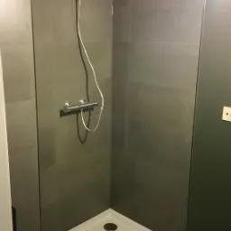 Nowoczesny prysznic z szarymi płytkami, białą brodzikiem i chromowaną armaturą, oświetlony od góry.