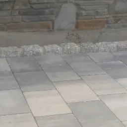 Ułożona szara kostka brukowa w Nowym Targu, widoczne obrzeża z kostki granitowej i fragment kamiennego muru w tle.