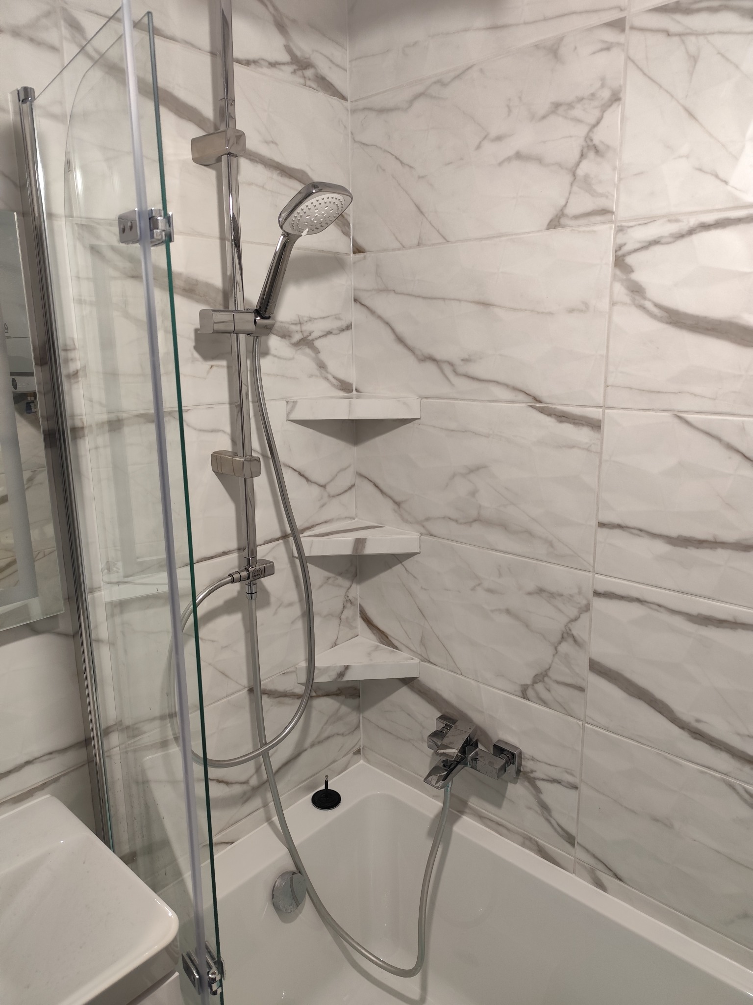 Wykończona łazienka z wanną, kabiną prysznicową i marmurowymi płytkami ściennymi z półkami narożnymi.