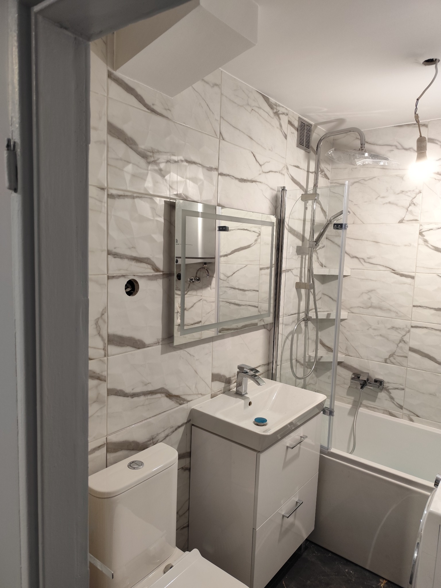 Wykończona łazienka w bieli i szarości z marmurkowymi płytkami, wiszącą szafką z umywalką, toaletą i kabiną prysznicową z deszczownicą.
