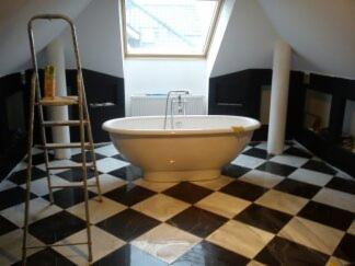 Łazienka na poddaszu z wanną wolnostojącą i czarno-białą szachownicą na podłodze. Drabina oparta o ścianę, okno dachowe. Wykończenie w stylu klasycznym.