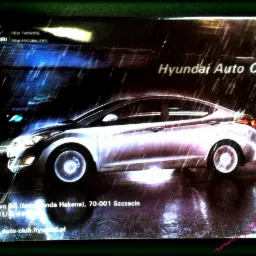 Plakat Hyundai Auto Club: srebrny samoch&oacute;d w deszczu, dynamiczne oświetlenie, adres w Szczecinie. Nowoczesny design, efekt mokrej nawierzchni.