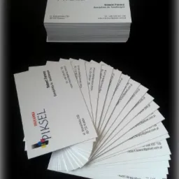 Stos wizytówek firmy Piskel ułożonych wachlarzowo i w stos. Wizytówki z danymi kontaktowymi Roberta Ferenca, specjalisty ds. handlowych, na czarnym tle.