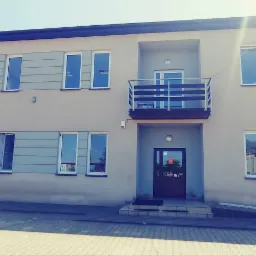 Dwupiętrowy budynek biurowy z balkonem i licznymi oknami, widok z zewnątrz w słoneczny dzień.