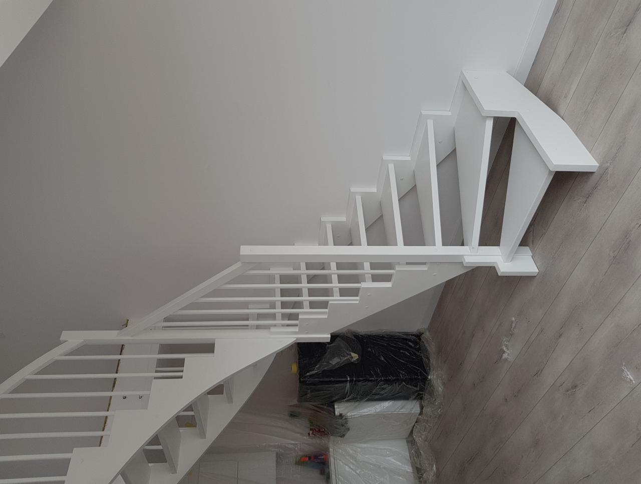 Białe, ażurowe schody z drewnianymi stopniami i barierką, widok z góry, pod schodami zabezpieczone folią malarską materiały budowlane.