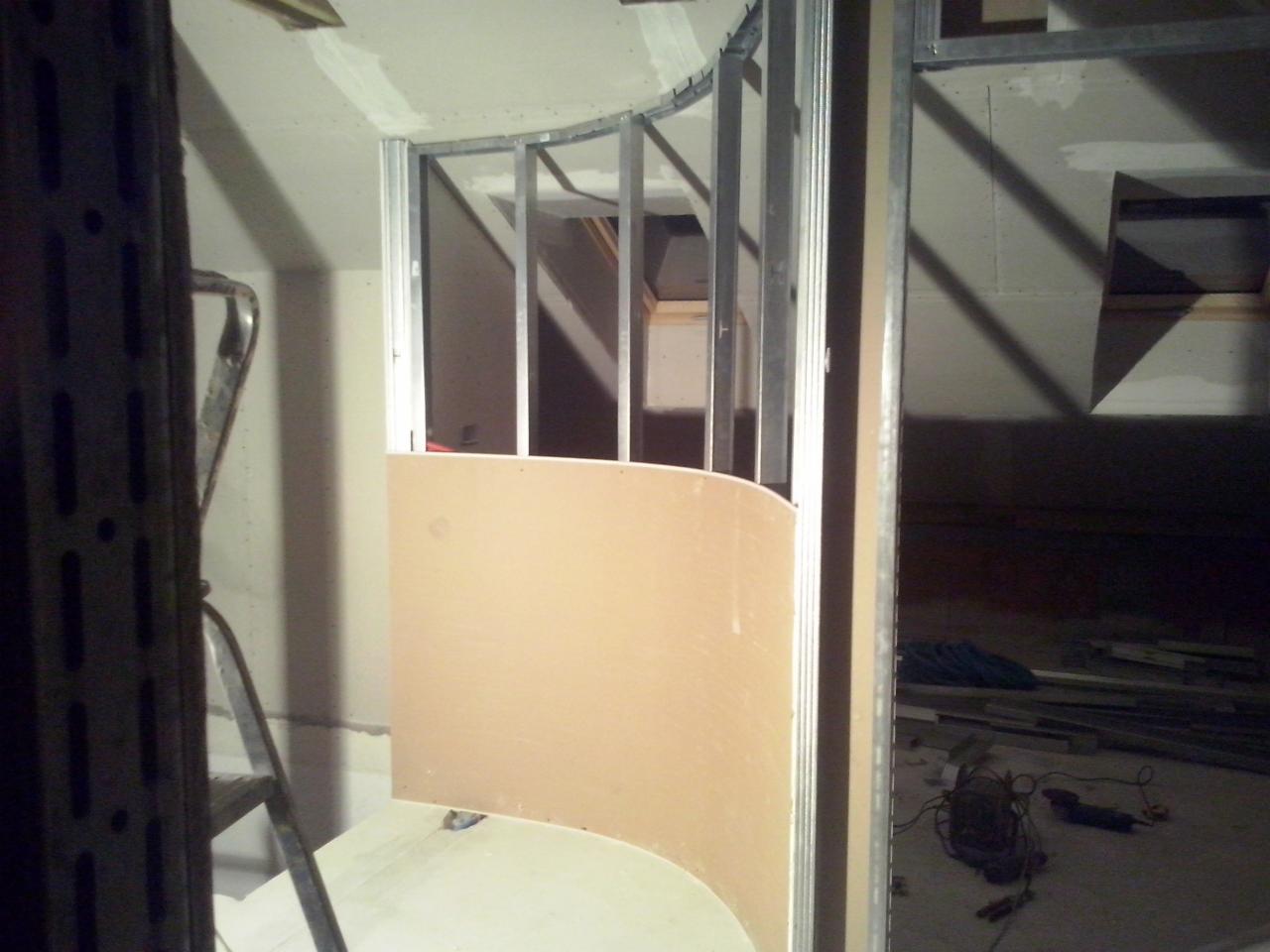 Kształtowanie ściany działowej z płyt gipsowo-kartonowych na metalowym stelażu. Widoczne narzędzia i materiały budowlane w surowym wnętrzu.