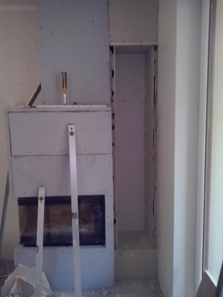 Wnętrze w trakcie zabudowy kominka płytami gipsowo-kartonowymi, widoczne poziomice i narzędzia. Etap prac wykończeniowych.