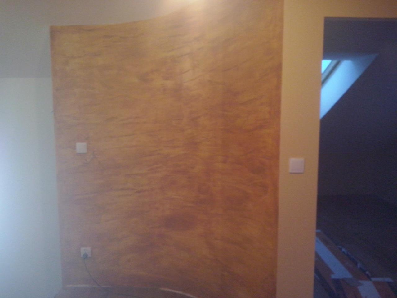 Dekoracyjna ściana w odcieniach brązu z efektem marmuru, widoczny fragment gniazdka elektrycznego i włącznika światła, fragment ościeżnicy drzwiowej.