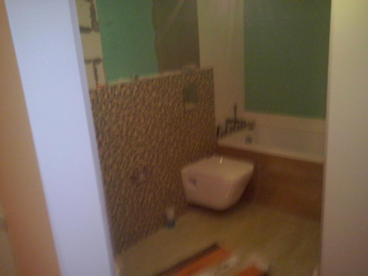 Remont łazienki w trakcie: częściowo wykończone płytki na ścianie, pomalowane ściany na zielono, zamontowana wanna i toaleta. Widoczne niedociągnięcia.